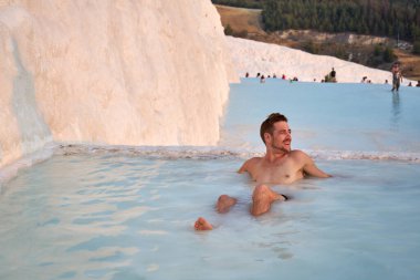 Pamukkale Doğal Parkı 'nda Türkiye' de beyaz travertin arasında yüzen mutlu bir gezgin. Genç adam Pamukkale doğal parkında güzel manzaralı bir havuzda dinleniyor..                      
