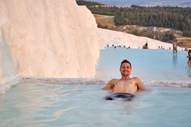 Pamukkale Doğal Parkı 'nda Türkiye' de beyaz travertin arasında yüzen mutlu bir gezgin. Genç adam Pamukkale doğal parkında güzel manzaralı bir havuzda dinleniyor..                      