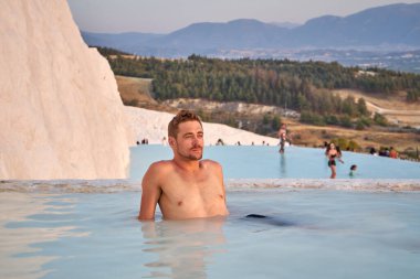 Pamukkale Doğal Parkı 'nda Türkiye' de beyaz travertin arasında yüzen mutlu bir gezgin. Genç adam Pamukkale doğal parkında güzel manzaralı bir havuzda dinleniyor..                      