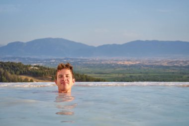 Türkiye 'de Pamukkale traverteni, manzaranın tadını çıkaran bir adam. Pamukkale Doğal Parkı 'nda yüzen ve güzel bir gün batımına bakan bir gezgin. Pamukkale' de dinlenen genç bir adam.              
