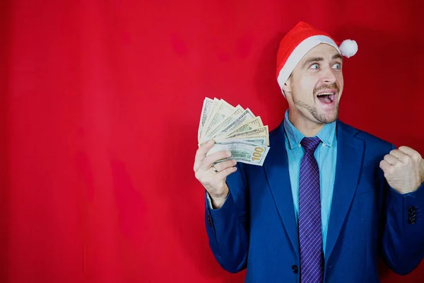 戴着红底礼帽的快乐商人 头戴圣诞礼帽的男性企业家持有美元钞票和新年彩券 圣诞老人帽 里兴奋的家伙拿着美元现金 — 图库照片