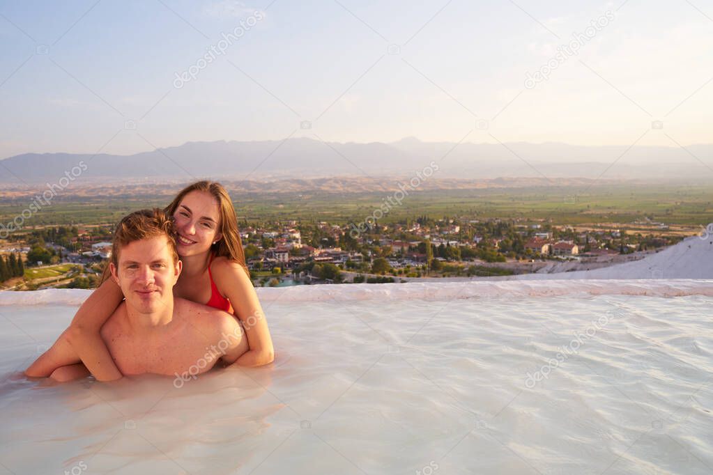 Loving couple at swimming pool in Pamukkale - St.Valentines Day concept.Lovers at sunset enjoing beautiful mountains view on their romantic journey.                                               