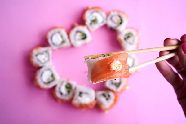 Sushi Rolls Salmon Heart Shape Woman Hand Chopsticks Pink Background 免版税图库照片