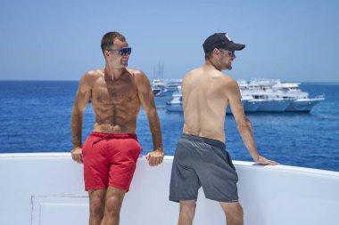 İki sportif erkek arkadaş yatta eğleniyor. Erkekler yaz tatilini yelkenli gezisinde geçiriyorlar. Su sporu tatili, yaz tatili. Tatil, boş zaman, yaşam tarzı konsepti 