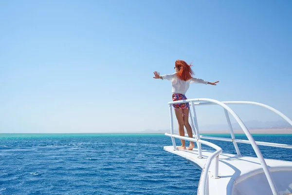 年轻的红头发姑娘躺在她的白色游艇的边缘 胳膊伸向不同的方向 享受着风的流动 自由和暑假的概念 图库图片