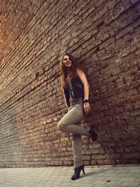 Linda chica con el pelo rojo de pie cerca de la pared de ladrillo —  Fotos de Stock