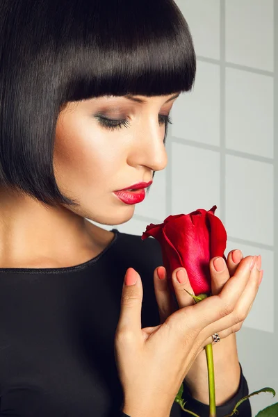 Gorgeous adult brunette with red rose on gray background in stud — Stock Photo, Image