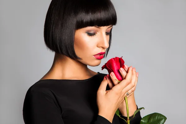 Beauty adult girl with red rose looking down in studio on gray b — Stock Photo, Image