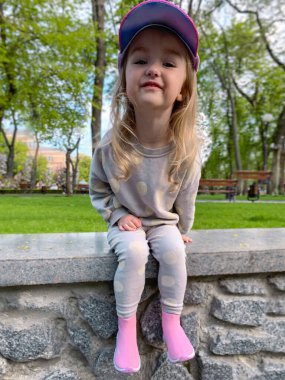 Eğlenceli küçük kız parkta oturur ve dışarıda kameraya gülümser.