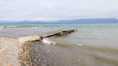 Dalgalar kıyıya sert vurur ve antik iskelenin kalıntılarını dağıtır. Ufuk uzaklardan görülebilir..