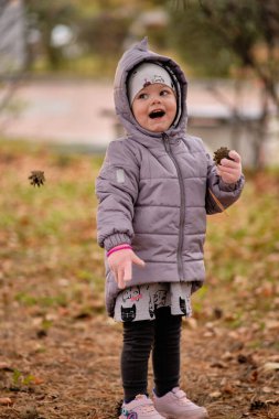 Dinozor ceketli küçük bir kız sonbahar yapraklarıyla oynuyor.