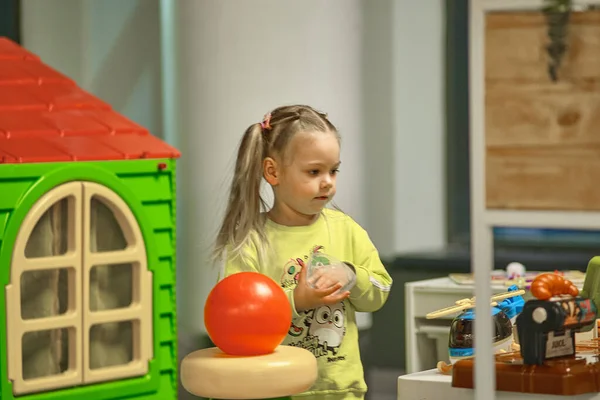 Een schattig klein meisje met paardenstaarten op haar hoofd speelt in een kinderstad. — Stockfoto