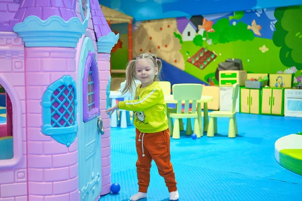 Een schattig klein meisje met paardenstaarten op haar hoofd speelt in een kinderstad. — Stockfoto