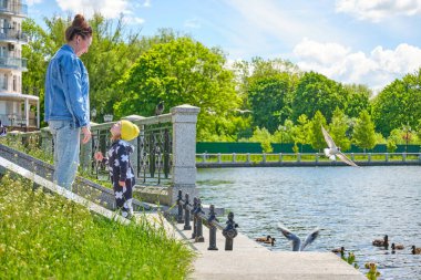 Anne ve kızı, şehrin göletindeki ördek ve martılara ekmek kırıntıları yediriyor..