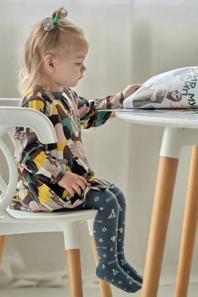 かわいいです女の子ともにポニーテール上彼女の頭読みます雑誌座っている上の椅子にテーブル ストック画像
