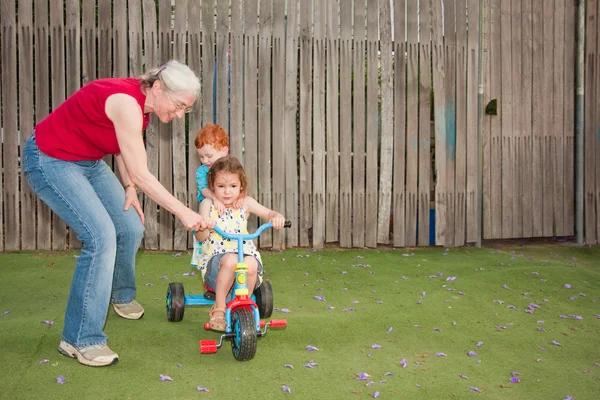 Büyükanne Trike binmek çocuklara yardım — Stok fotoğraf