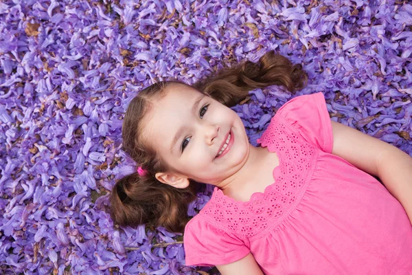 Meisje kind liggen onder paarse bloemen — Stockfoto