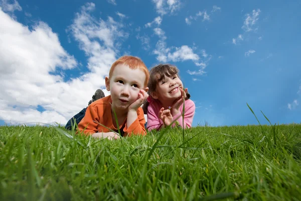 Divertidos niños felices acostados en la hierba con el cielo azul — Foto de Stock