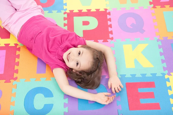 Smiling girl lying on alphabet tiles — Stock Photo, Image