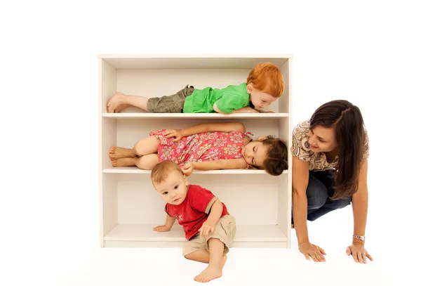 Crianças brincando de esconde e procura com a mãe na estante Fotos De Bancos De Imagens