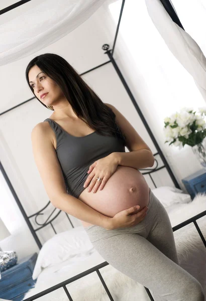 Bruna donna sorridente mostra pancia incinta in piedi vicino baldacchino — Foto Stock