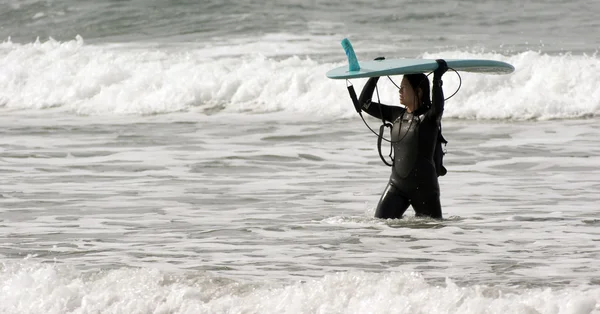 Seriöse Surf-Boarderin trägt ihr Surfbrett durch die Brandung — Stockfoto