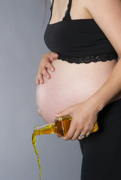Очень беременная женщина разливает бутылку крепкого алкогольного виски — стоковое фото