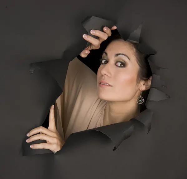 Vacker brunett kvinna ser ut i sidled genom slits hål — Stockfoto