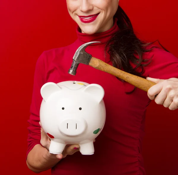Femme souriante en rouge tient le marteau au-dessus de la tirelire épargne — Photo
