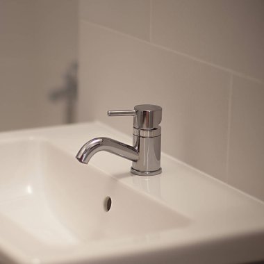 Beyaz lavabonun arka planında küveti olan musluk, seçici bir odak noktası.