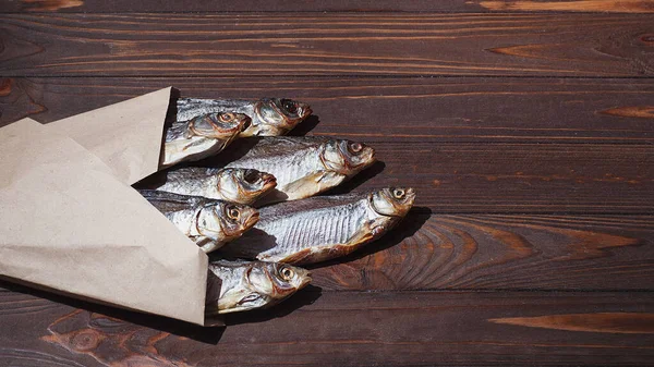 Gros plan de poissons séchés sur un fond en bois foncé dans du papier artisanal. place pour le texte. Orientation horizontale. — Photo