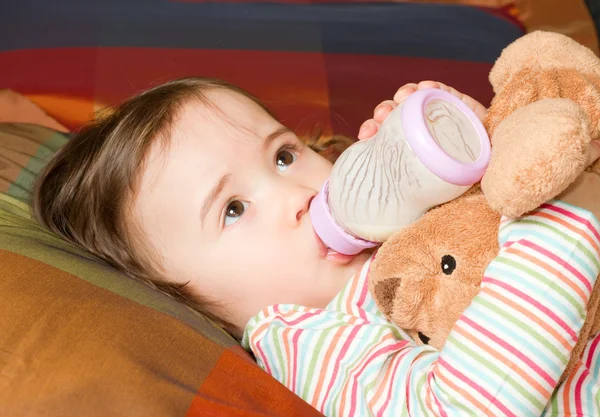 Pretty baby girl with infant formula in bottle on bad. The concept of chil — Stock Photo, Image