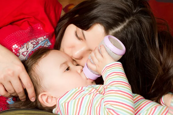 Ung mamma matar barn flicka med en flaska med välling på dåliga. den — Stockfoto