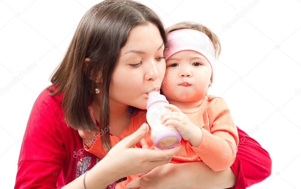 Young mother feeds child girl with a bottle with infant formula on bad. The