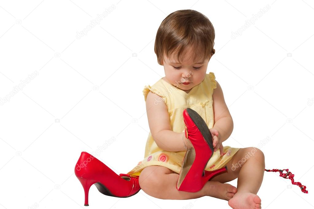 Little girl-child trying on mother s big red shoes on a white background