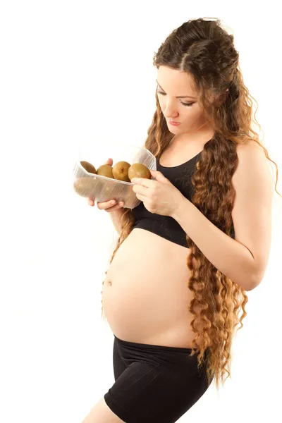 Ung gravid kvinna i sportkläder med kiwi på vit bakgrund diet en — Stockfoto