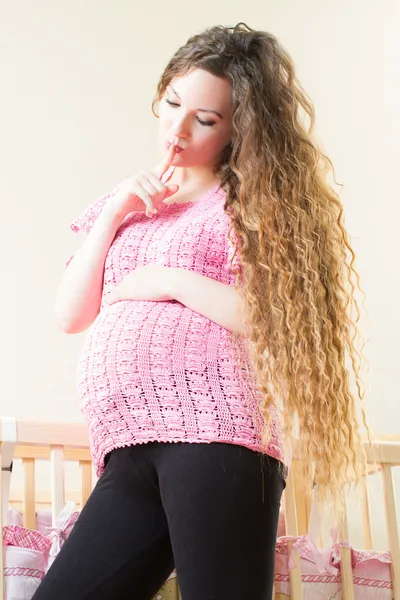 Беременная женщина с длинными волосами возле кроватки — стоковое фото