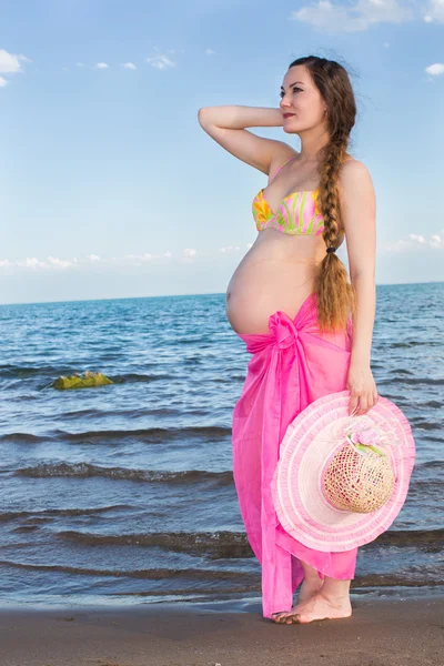 Joyeux belle femme enceinte en maillot de bain et chapeau de marche, relaxant à bea — Photo