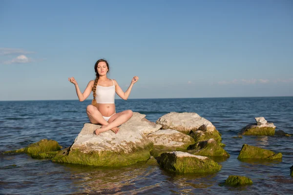 Беременная женщина с длинными волосами медитирует в позе йоги на море — стоковое фото