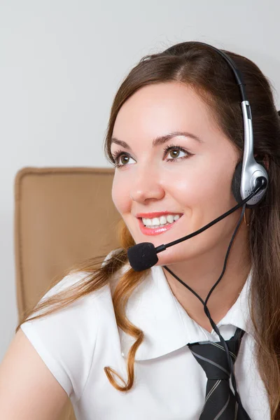 Kuulokkeet. Asiakaspalvelun operaattori nainen, jolla on kuulokkeet hymyillen toimistossa — kuvapankkivalokuva