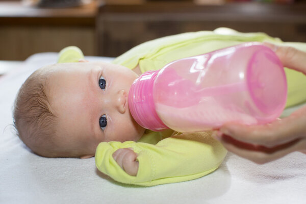 Newborn baby girl with a bottle of milk. The concept of food and parenting