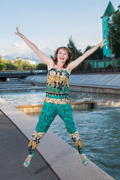 Fun young woman jumping on embankment in summer in city — Stock Photo, Image