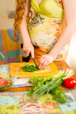 pregnant woman s hands and belly cutting on kitchen with healthy food The concept of food and a healthy lifestyle clipart