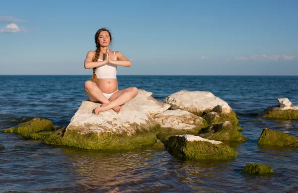Pregnant woman in sports bra doing exercise in relaxation on yoga pose on sea — Stock Photo, Image