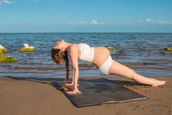 Pregnant woman in sports bra doing exercise in relaxation on yoga pose on sea — Stock Photo, Image