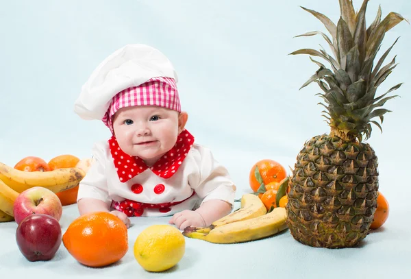 Retrato de un bebé sonriente con un sombrero de chef rodeado de frutas Úsalo para un niño, concepto de comida saludable — Foto de Stock