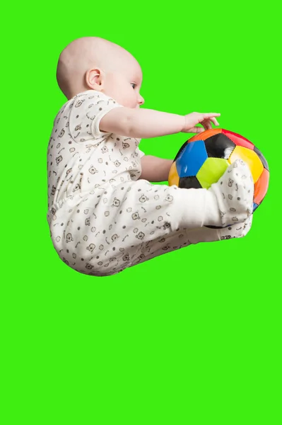 Малыш играет с футбольным мячом на зеленом фоне. Дети и младенцы — стоковое фото