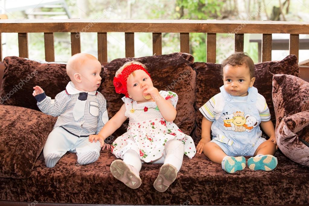 Small three children: black american, caucasian boys and russian baby girl siting up on sofa