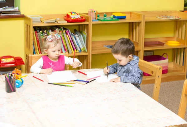 Zwei kleine Kinder malen mit Buntstiften in der Vorschule am Tisch. Kleine Mädchen und Jungen zeichnen im Kindergarten — Stockfoto