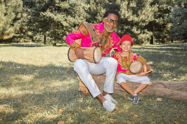 Handsome African man in a national costume plays an ethnic drum, djembe together with son.
